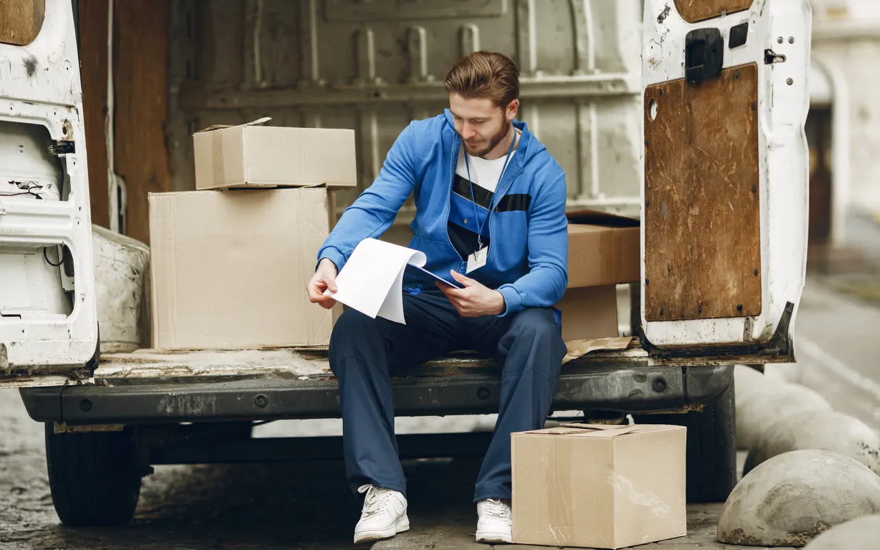 A delivery worker reviewing paperwork beside boxes mirrors a painter reconciling job costs against an underquoted small job.