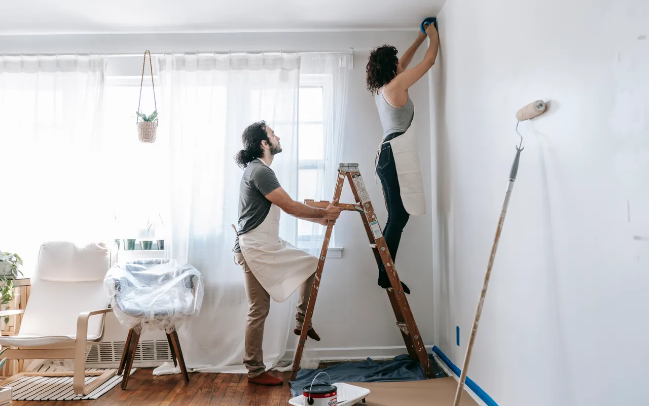 A couple preparing to paint their lived-in room signals the friction and coordination overhead that drives occupied-home labour costs higher.
