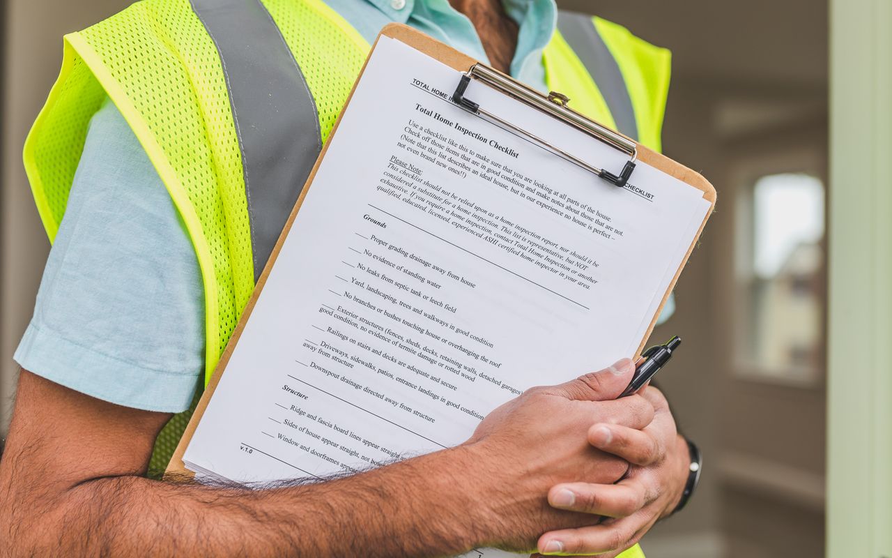 A hi-vis-vested worker reviews a detailed checklist on a clipboard at a construction site, mirroring the structured inspection and scheduling process central to a multi-year painting program.