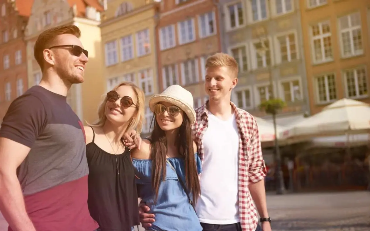 Četvoro prijatelja nasmejanih sa naočarama za sunce, šetaju fradom zagrljeni