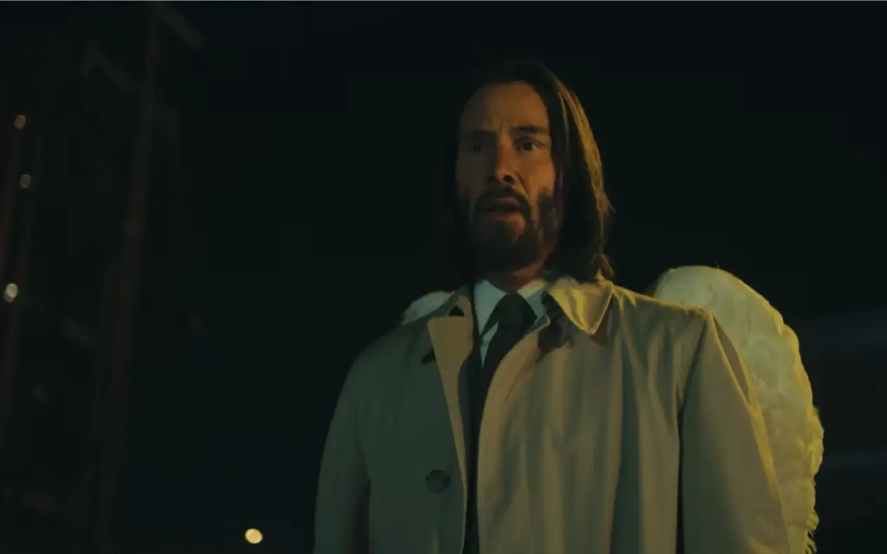 Keanu Rives u bež mantilu i sa anđeoskim krilima stoji i posmatra prizor sa zabrinutim izrazom lica