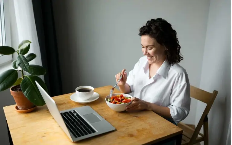 Žena sa hranom tokom posla Žena jede saltu pred računarom zbog manjka vremena