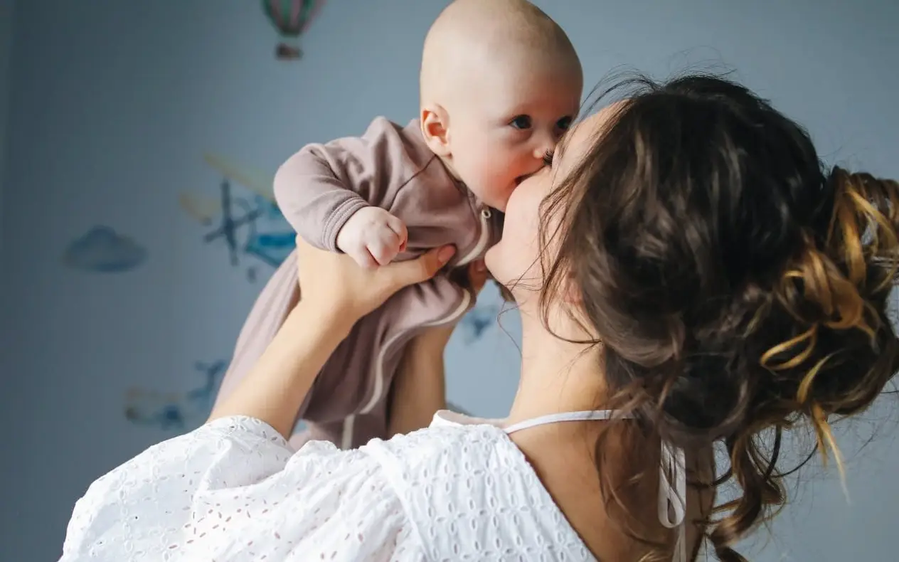 Beba grize majku za nos dok ga visoko drži u naručju i sa osmehom na licu