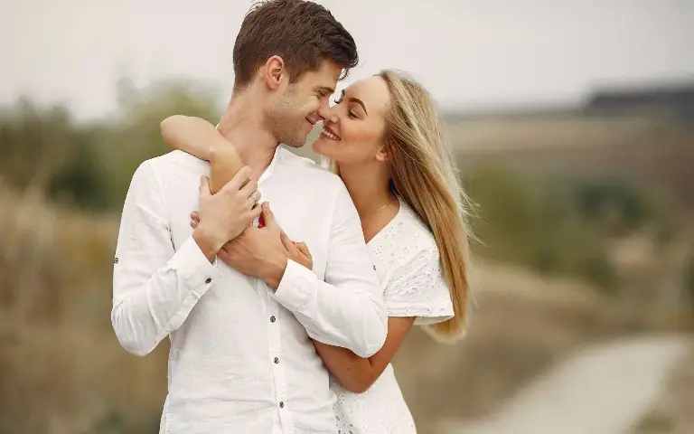 Zaljubljeni par Dvojhe mladih obučeni u belo zaljubljeno se gledaju i grle dok šetaju prirodom