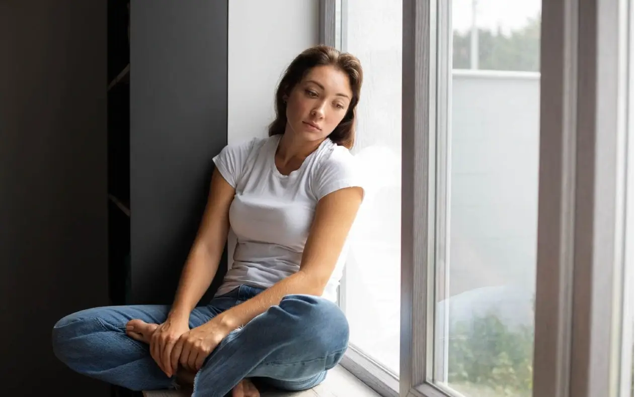 Tužna devojka sedi pored prozora i razmišlja