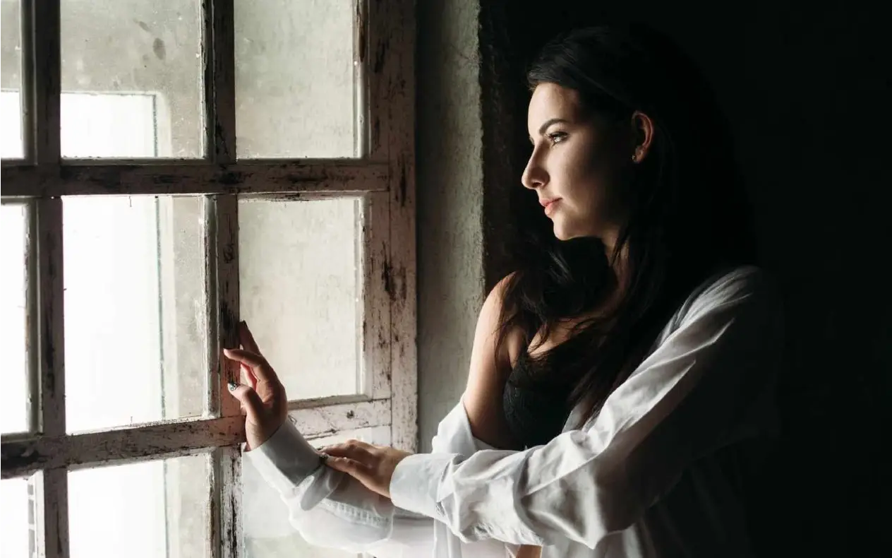 Žena sedi sama pored prozora i gleda u daljinu, simbol usamljenosti i unutrašnje borbe