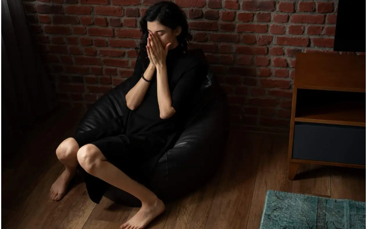 Zamišljena žena sedi sama i drži se za glavu, simbol lične ispovesti i unutrašnje borbe
