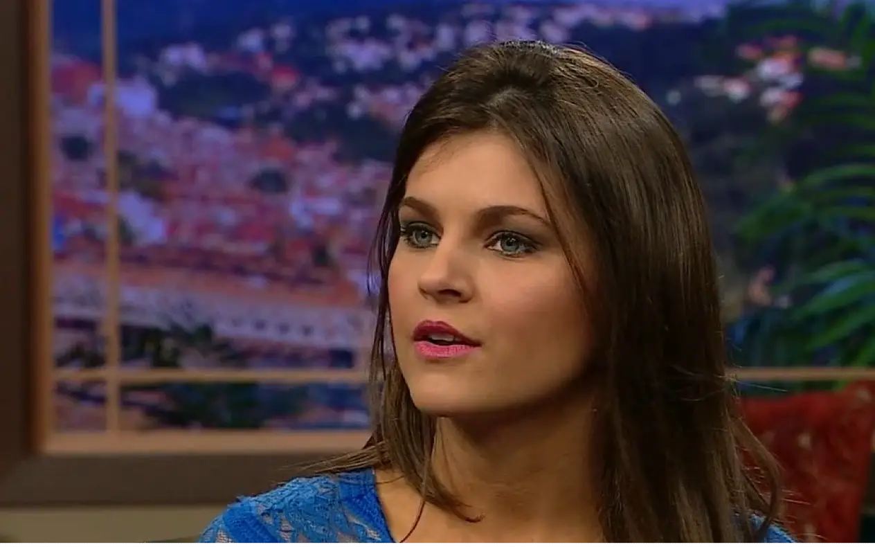 Valerie Gatto, brineta u plavoj haljini, tokom televizijskog intervjua sa pozadinom koja prikazuje panoramu grada.