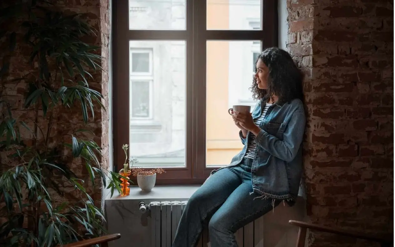 Žena sedi pored prozora zamišljena