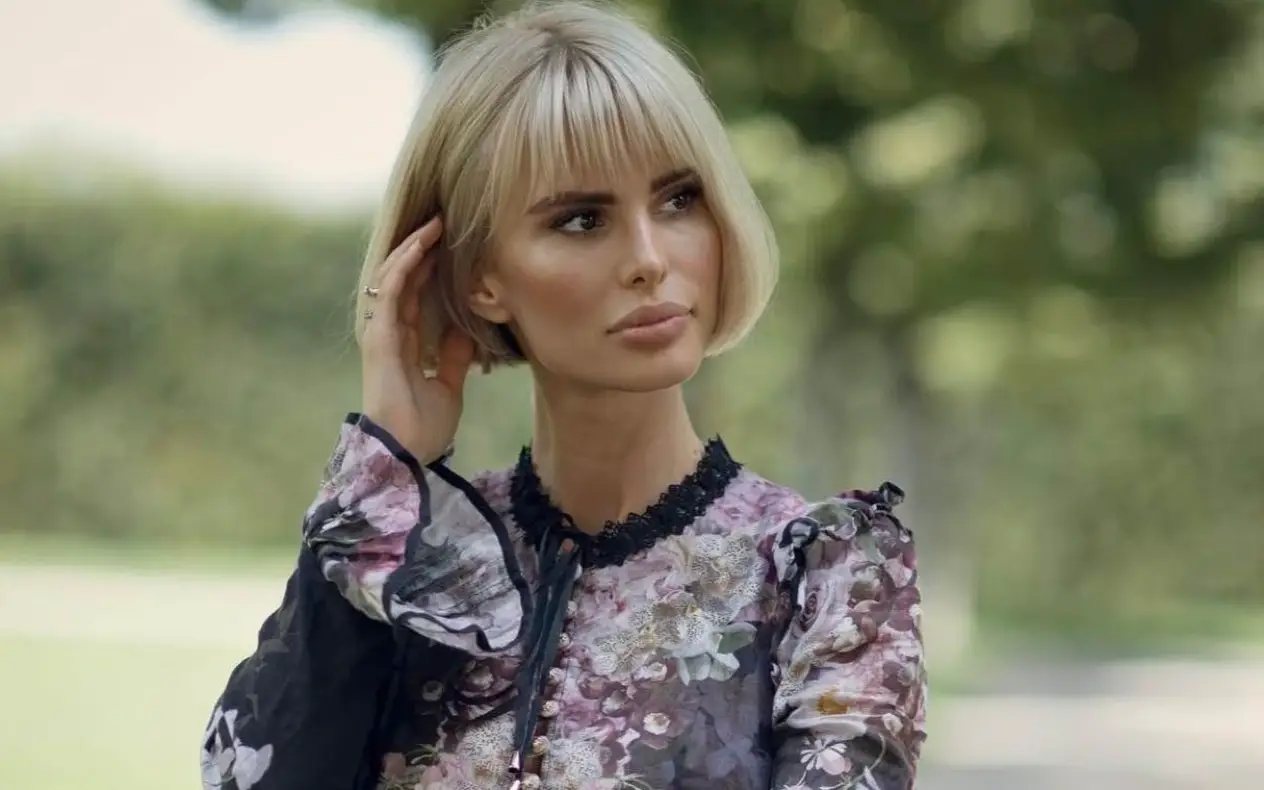 Carolina Miškić u crnoj cvettnoj lanenoj haljini sa zamišljenim pogledom i rukom u kosi