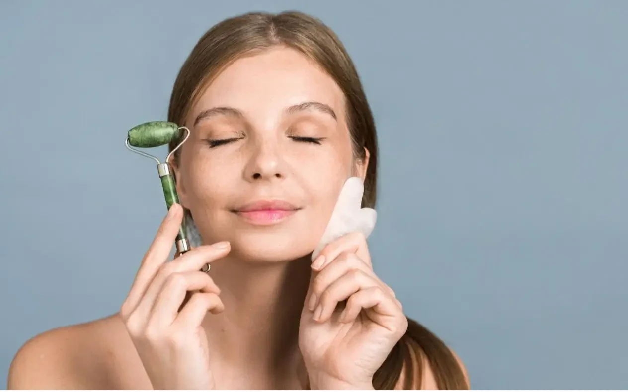 Gua Sha masaža i valjak od žada za negu lica Žena koristi Gua Sha kamen od žada za nežnu masažu lica kao deo svakodnevne rutine nege kože.
