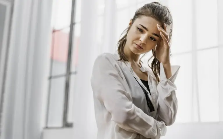 Umorna žena se drži za glavu Premorena žena koja se drži za glavu i stoji pored prozora