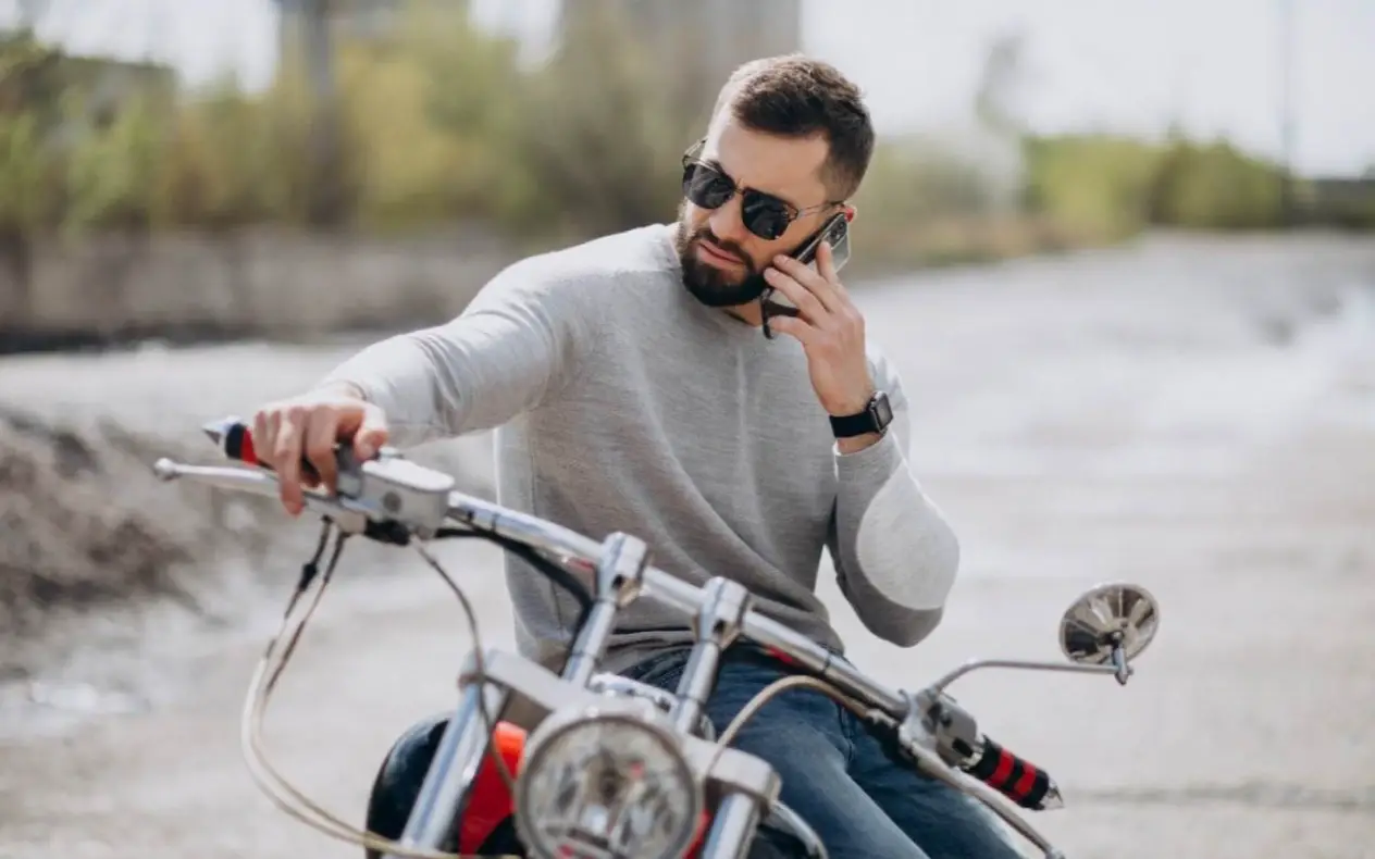 Muškarac na motoru Muškarac na motoru u sivom džemperu i naočarama priča telefonom
