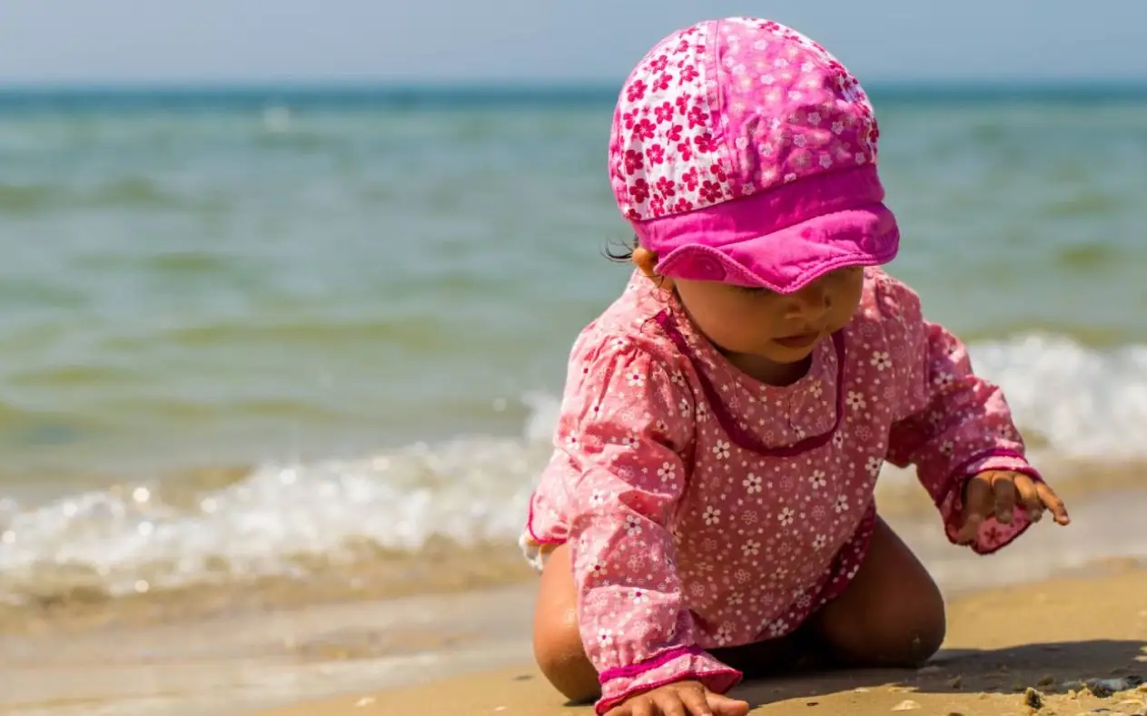 Beba na plaži sa šeširom i zaštitnom kremom za sunce
