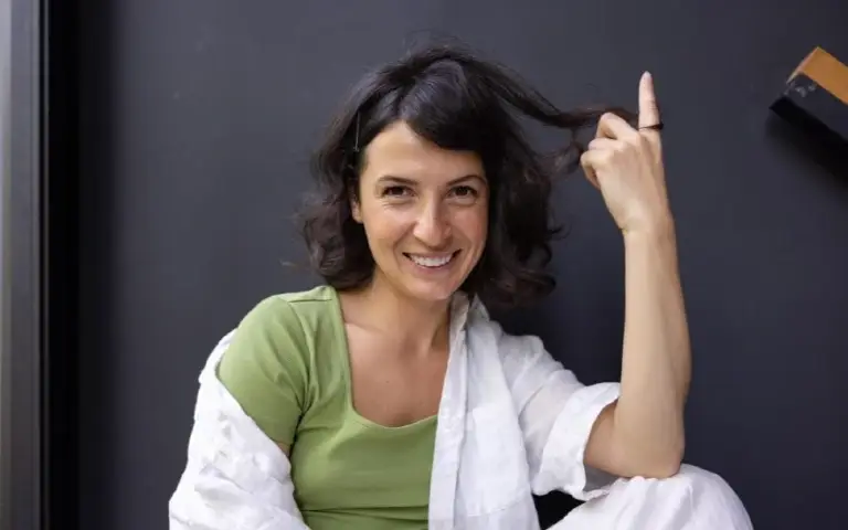 Nasmejana žena sedi i gleda u kameru