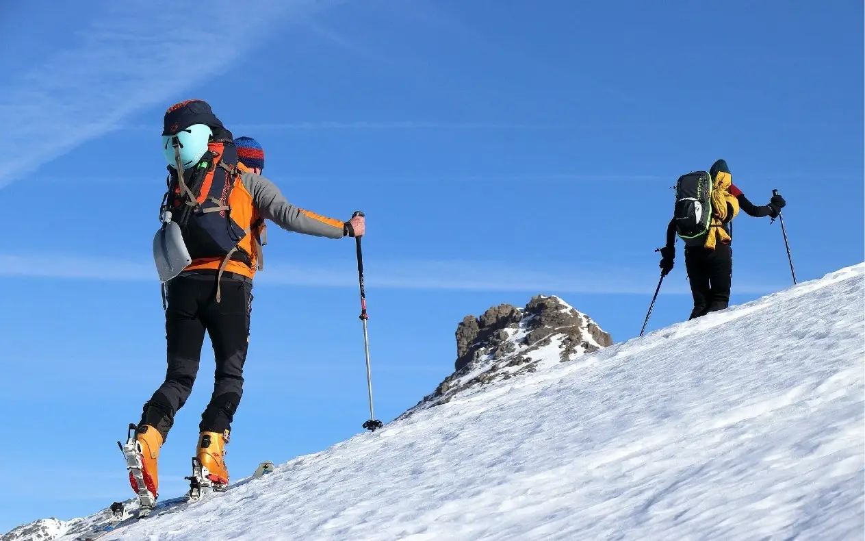 Skijaši sa punom skijaškom opremom se penju uz planinu pod snegom