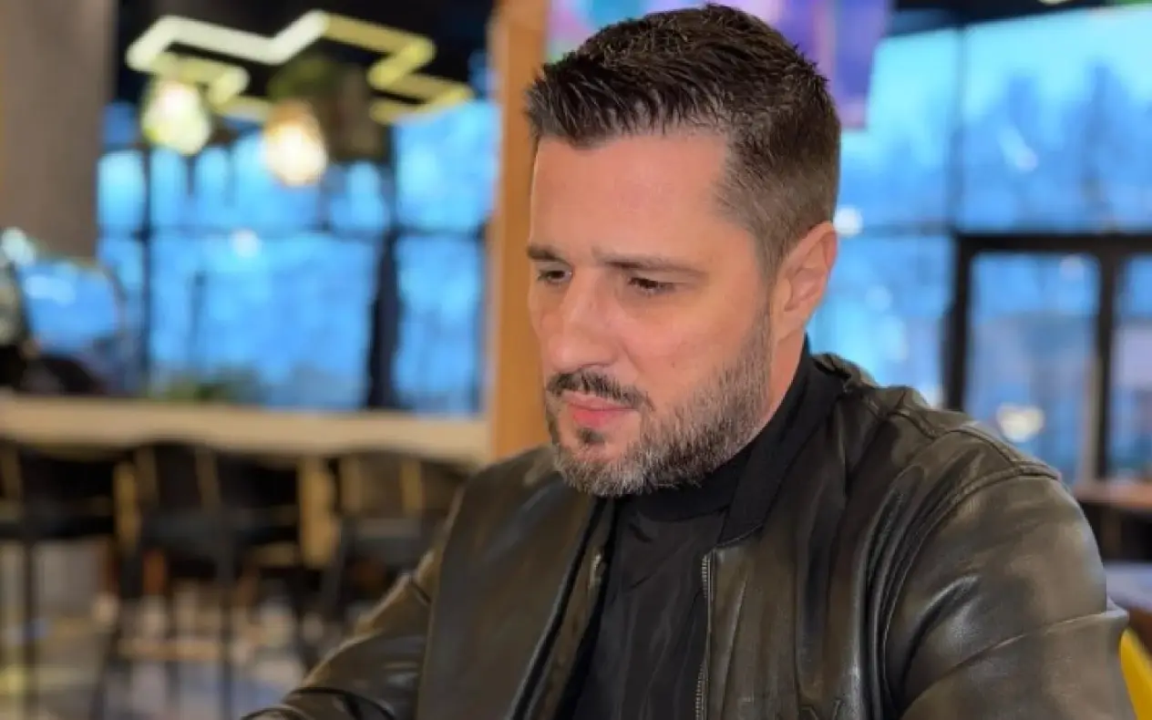 Marko Miljković sa ozbiljnim izrzazom lica sedi za stolom i gleda u telefon