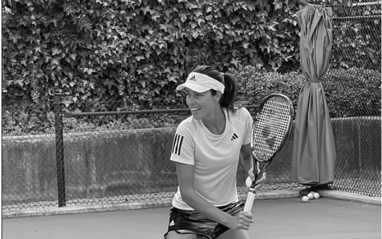 Ana Ivanović na teniskom terenu u beloj sportskoj opremi, u trenutku pripreme za udarac.