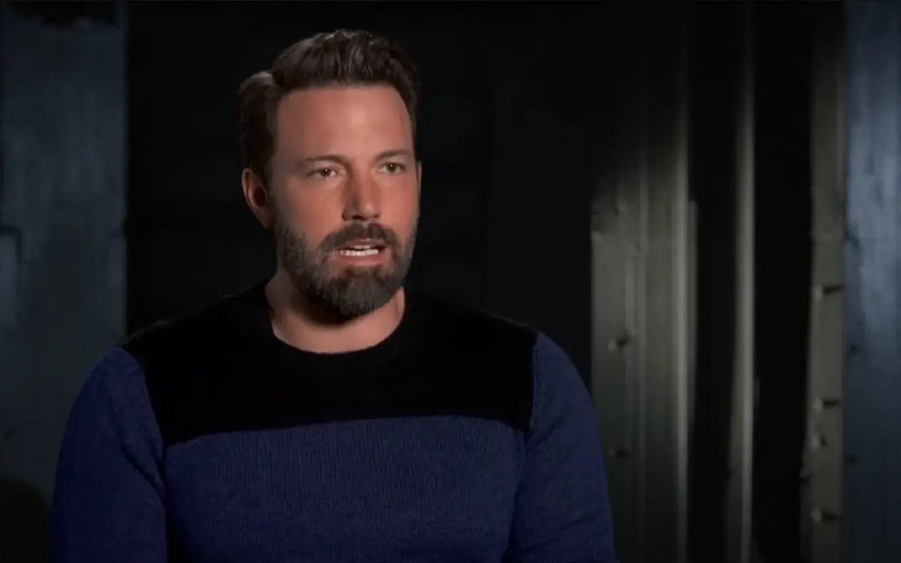 Ben Affleck u emisiji Ben Affleck u teget crnom džemperu sedeći u studiju tokom televizijskog intervjua, s noćnim gradskim pejzažom u pozadini.