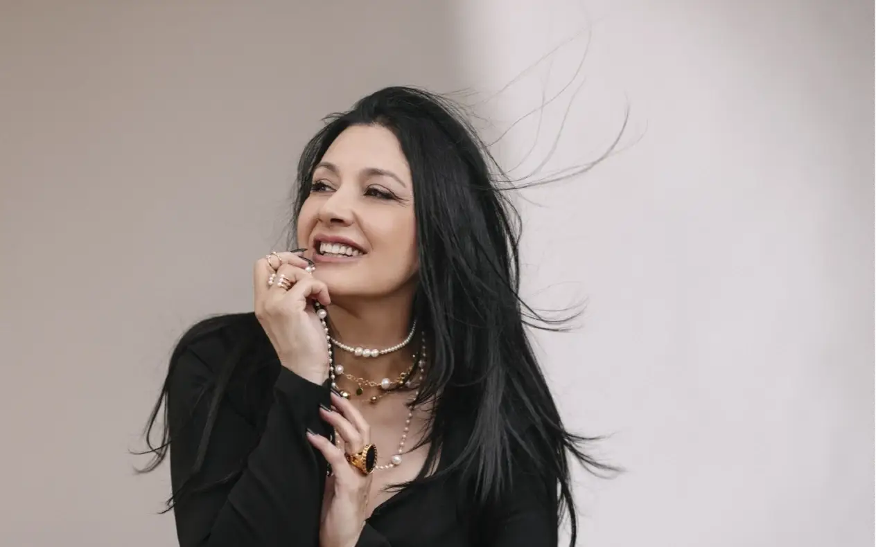 Kaliopi pozira sa širokim osmehom na licu, nakitom oko vrata dok joj se kosa viori