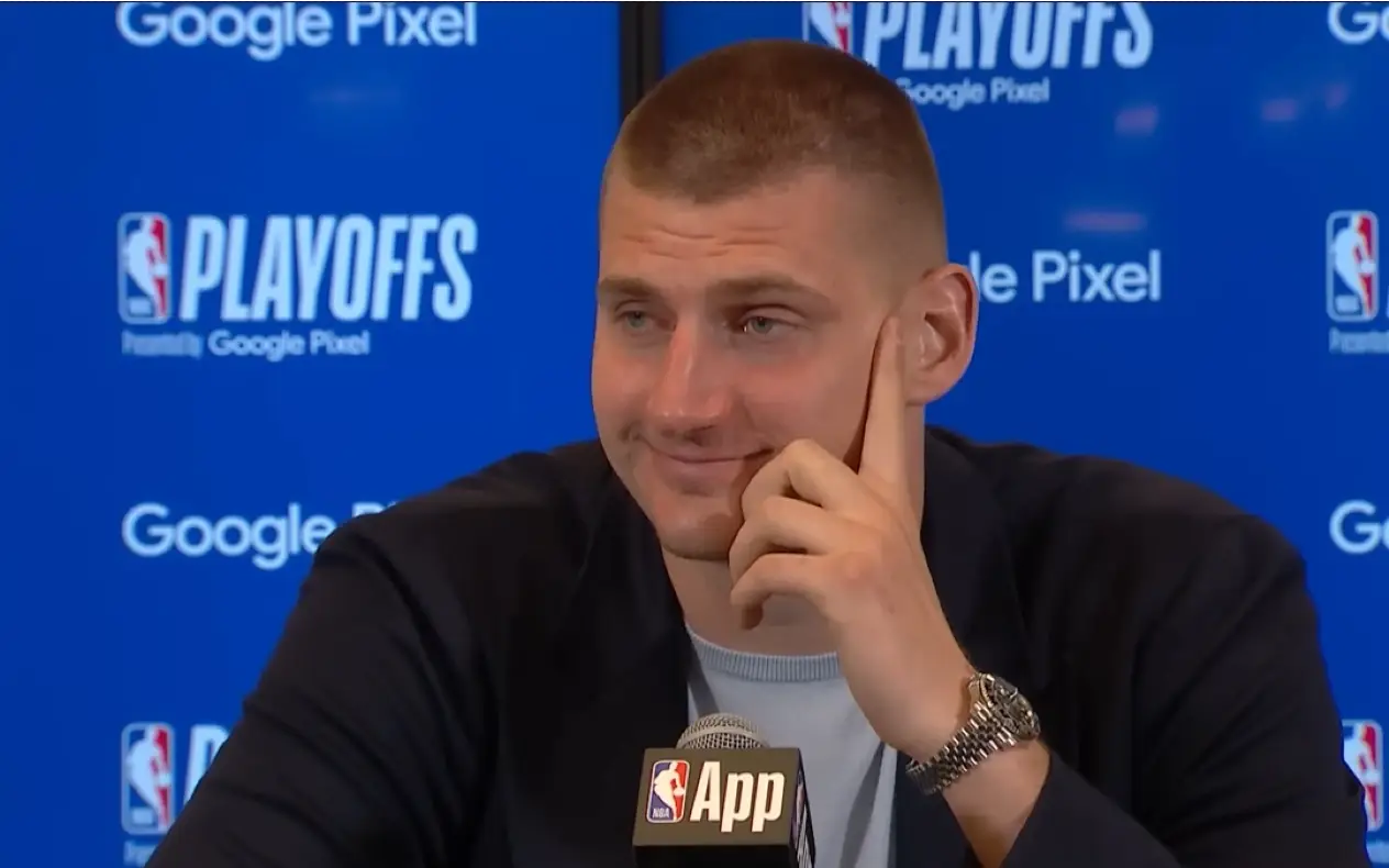 Nikola Jokić sa osmehom sedi na konferenciji za medije, u pozadini natpisi "NBA Playoffs" i "Google Pixel"