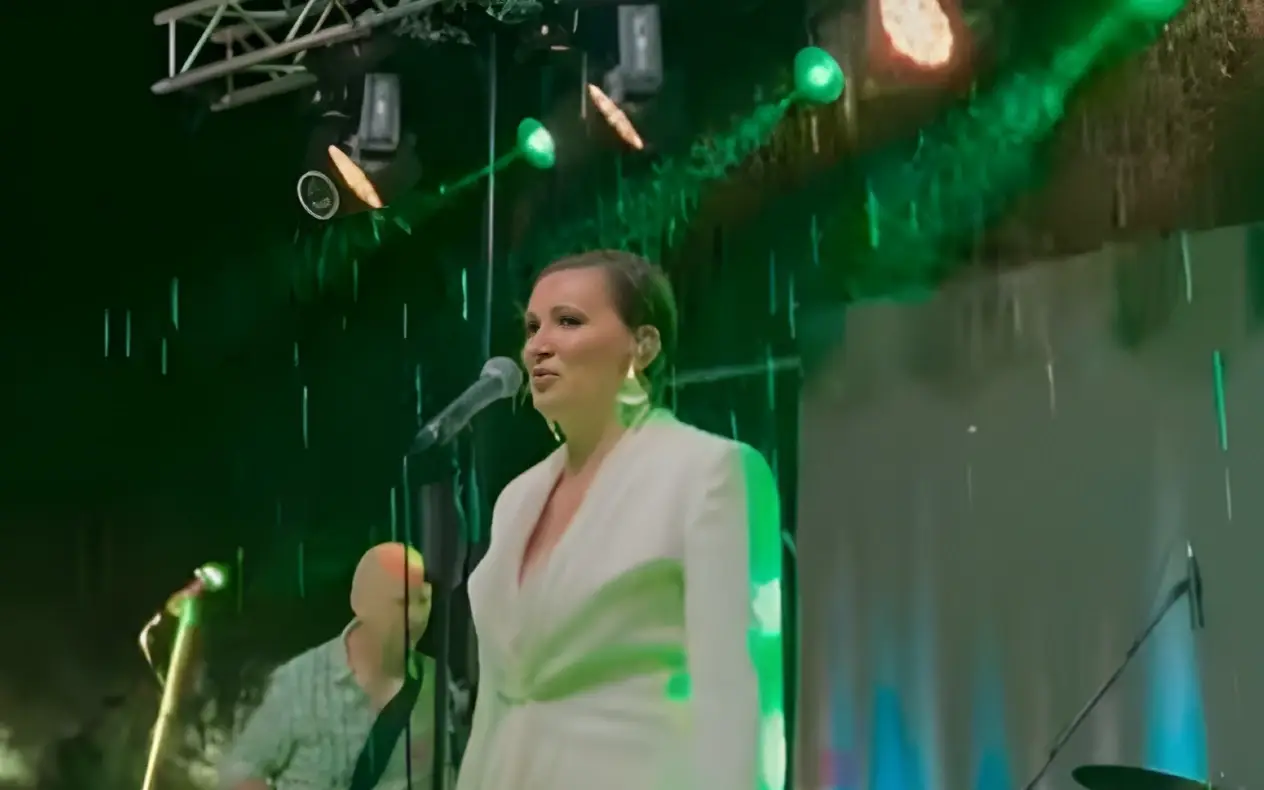 Nina Badrić u belom kompletu i sa zalizanom kratkom kosom peva na kiši