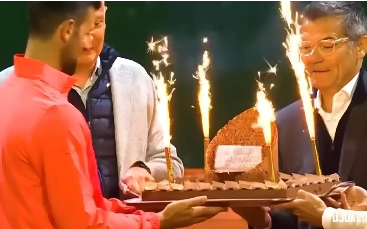 Novak Đoković u crvenoj trenerci dobija rođendansku tortu na terenu nakon pobede u četvrtfinalu meča u Ženevi 