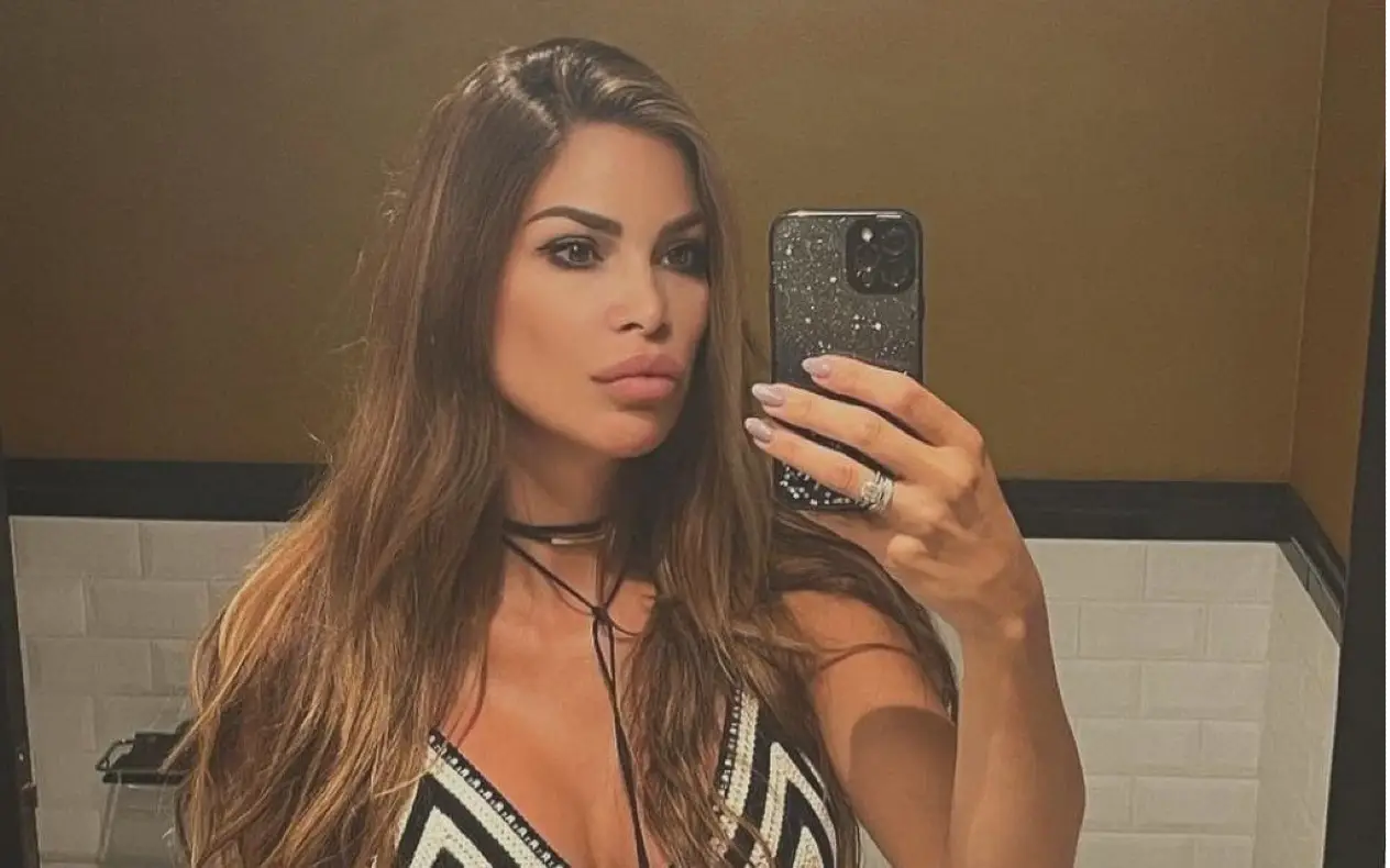 Olja Crnogorac snima selfi u ogledalu, obučena u crno-belu haljinu sa dubokim dekolteom, sa dugom talasastom kosom i elegantnom šminkom.
