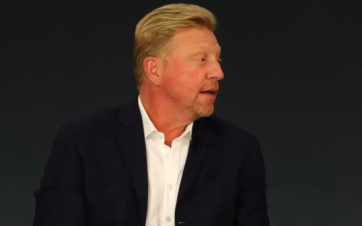 Boris Becker u tamnom odelu i beloj košulji tokom intervjua sa ozbiljnim izrazom lica