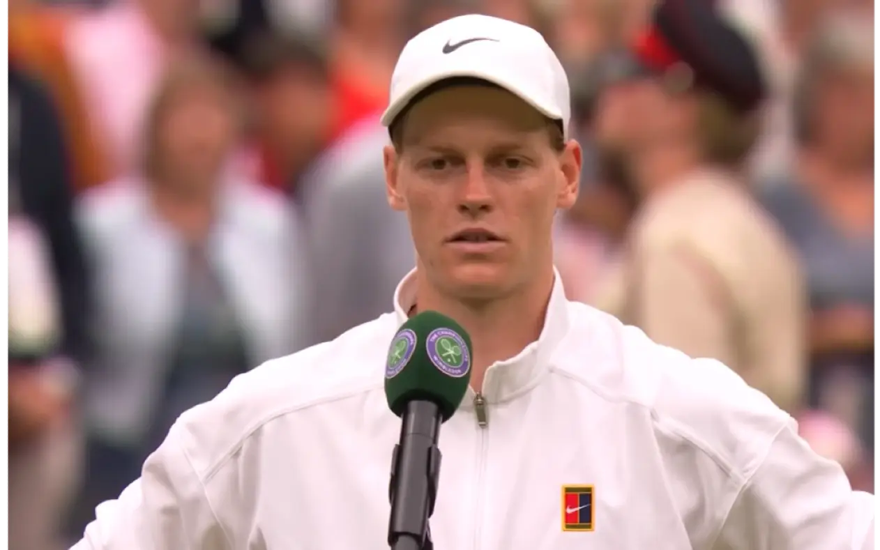 Jannik Sinner sedi pred mikrofonom na konferenciji za medije tokom Wimbledona u sportskoj dukserici.