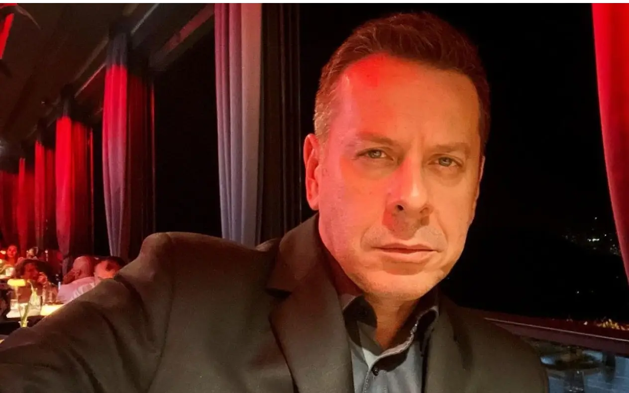 Vlado Georgiev u crnom odelu, prijatnom ambijentu sa ozbiljnim izrazom lica