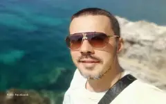 Bojan sa naočarima za sunce, osmehuje se dok pozira pored mora na steni