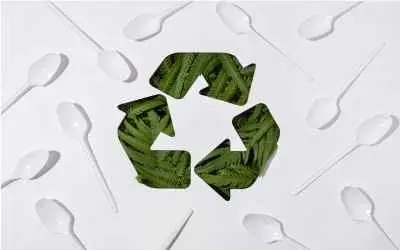 Simbol reciklaže sa zelenim lišćem okružen belim plastičnim kašikama na beloj pozadini