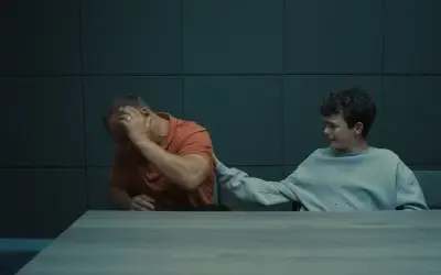 Dečak u sivoj dukserici udara muškarca u narandžastoj majici tokom ispitivanja u seriji Adolescence.