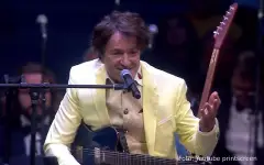 Goran Bregović u žutom odelu sa giratom i mikrofonom na koncertu