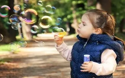 Devojčica prave balone od sapunice u teget prsluku na tufne