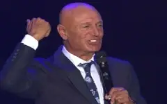 Šaban Šaulić u odelu sa podignutom pesnicom na koncertu i mikrofonom u ruci