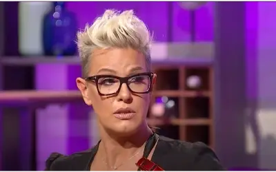 Tijana Dapčević u TV emisiji Pevačica Tijana Dapčević sa kratkom platinastom kosom i crnim naočarima, obučena u crnu bluzu, tokom gostovanja u televizijskoj emisiji sa ljubičastom rasvetom u pozadini.