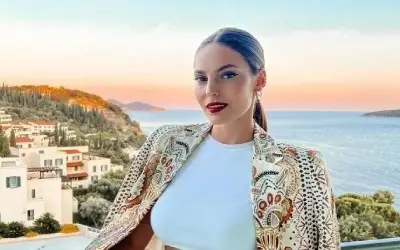 Džejla Ramović u šarenom sakou i beloj majici sa izrazito jakom šminkom i blagim osmehom na licu pozira pored mora