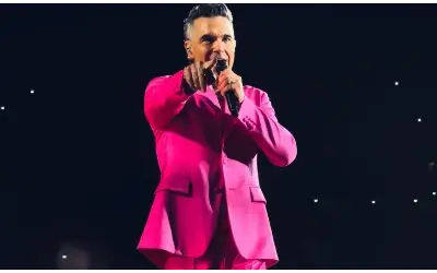 Robbie Williams nastupa na stadionu Ernst Happel u Beču, okružen svetlima i publikom.