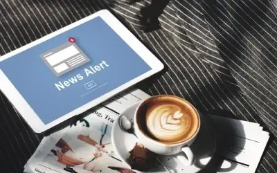Važne vesti – News Alert na ekranu tableta Tablet sa obaveštenjem o važnim vestima (News Alert) na stolu, pored šoljice kafe i novina.