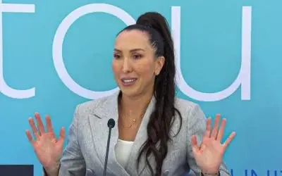 Jelena Janković na konferenciji Jelena Janković u sivom sakou, beloh majici sa raširenim rukama i blagim osmehom na licu