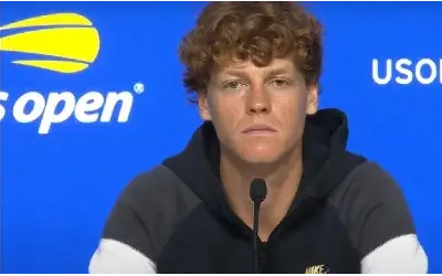 Jannik Sinner sedi pred mikrofonom na konferenciji za medije tokom US Opena, u sportskoj dukserici.