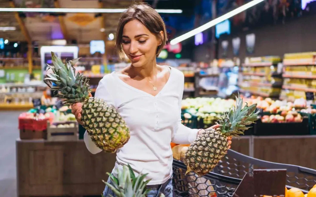 Žena sa kolicima drži anans Žena sa nekoliko punih kolica na kasi u prodavnici