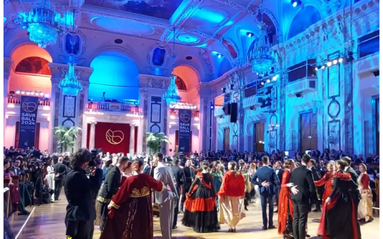 Učesnici Sava Balla 2024 plešu u raskošnoj dvorani sa osvetljenjem u plavim i crvenim tonovima, pod velikim kristalnim lusterima.