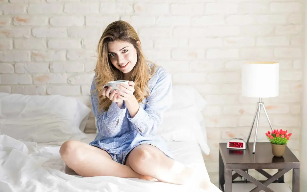 Mlada žena sedi na krevetu i pije kafu