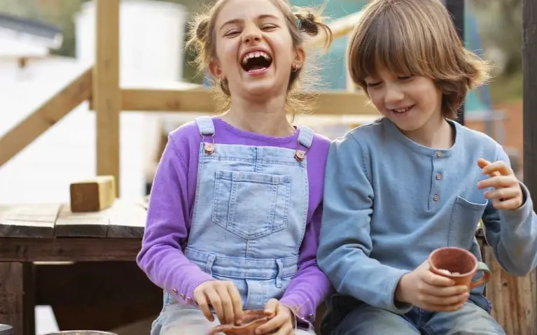 Nasmejana deca u parku sede jedno pored drugog i uživaju u druženju