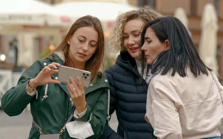 Grupa devojaka na ulici gleda u mobilni telefon dok jedna od njih pokazuje na ekran