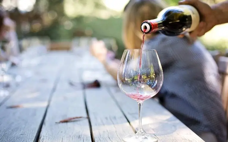 Čaša crnog vina Konobar sipa čašu crnog vina na drvenom stolu u prirodi