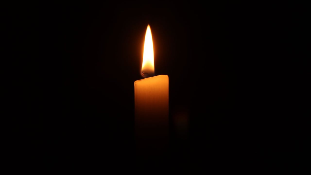 A single burning candle in the dark, casting a warm and serene glow.